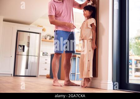 Il padre asiatico misura la figlia sulla scala della parete a casa come lei sta sulle punte Foto Stock