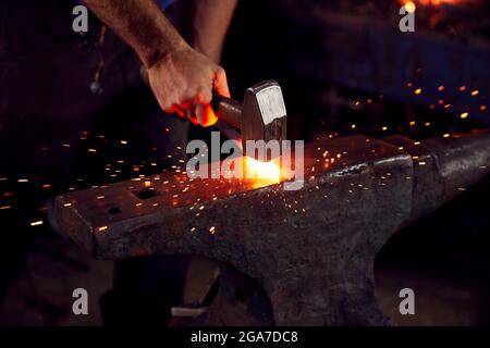 Primo piano di Male Blacksmith martellando metallo su incudine con Sparks Foto Stock