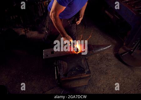 Primo piano di Male Blacksmith martellando metallo su incudine con Sparks Foto Stock