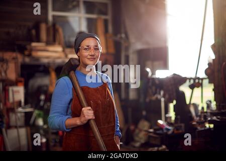 Ritratto di martello da presa Blacksmith femminile in piedi a Forge Foto Stock