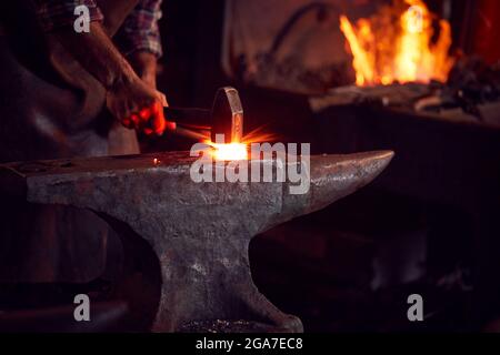 Primo piano di Male Blacksmith martellando metallo su incudine con Sparks Foto Stock