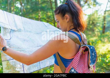 Giovane bella donna escursionista con zaino tenendo la mappa in estate Forest.female viaggiatore che controlla destinazione su map.Young femmina escursionista utilizzando la mappa per orien Foto Stock