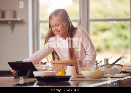 Ragazza che indossa Pajamas fare Pancakes in cucina a casa seguendo la ricetta su Digital Tablet Foto Stock