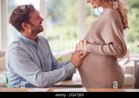 Primo piano di coppia con l'uomo che tocca lo stomaco delle donne incinte mentre si alza accanto a lui Foto Stock