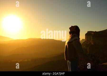 Vista laterale ritratto di una silhouette retroilluminata di una donna che respira aria fresca in montagna all'alba Foto Stock