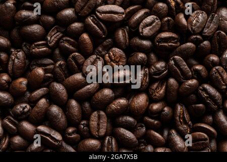 caffè marrone, consistenza dello sfondo, primo piano. Una macro foto di chicchi di caffè marrone fritti sul tavolo. Foto Stock