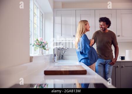 Coppia con la moglie incinta in cucina che parla e beve il caffè insieme Foto Stock
