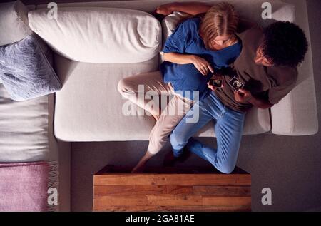 Vista dall'alto di coppia con donna incinta guardando le scansioni a ultrasuoni del bambino sul divano a casa Foto Stock