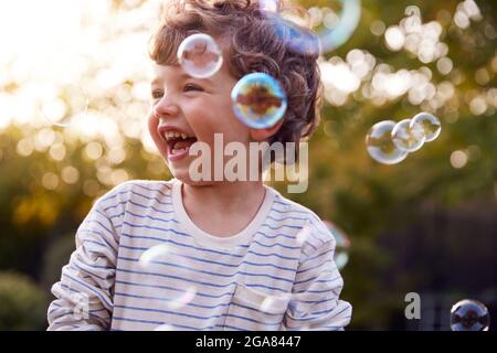 Young Boy divertirsi in Garden Chasing e scoppiare bolle Foto Stock