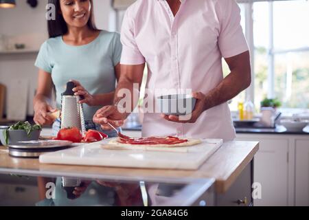 Uomo che diffonde salsa di pomodoro sulla base come coppia in cucina Casa preparare pizze fatte in casa insieme Foto Stock