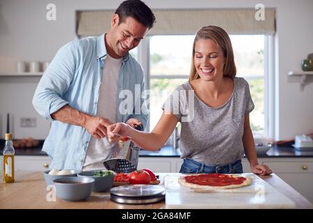 Donna che diffonde salsa di pomodoro sulla base come coppia in cucina Casa preparare pizze fatte in casa insieme Foto Stock