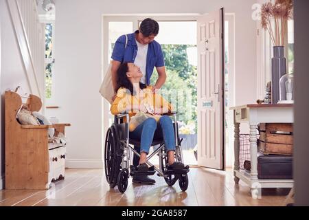 Uomo asiatico che spinge la moglie in sedia a rotelle a casa ritorno da Shopping viaggio con borsa Foto Stock