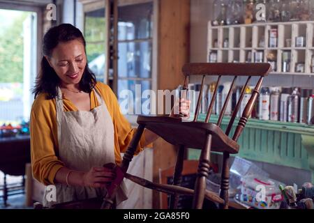 Mature Asian Woman Restoring Furniture in Workshop a casa Foto Stock