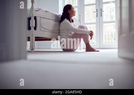 Infelice e depresso Donna asiatica matura in Pajamas seduta sul pavimento della camera da letto Foto Stock
