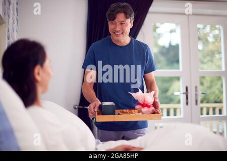 L'uomo asiatico maturo portando la colazione della moglie in letto per celebrare il compleanno o l'anniversario Foto Stock