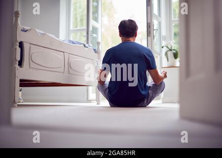 Vista posteriore della donna asiatica matura in Pajamas seduta sul pavimento della camera da letto meditando in posa Yoga Foto Stock