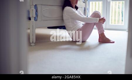 Primo piano di infelice e depressa donna asiatica matura in Pajamas seduta sul pavimento della camera da letto Foto Stock