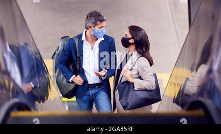 Coppia di lavoro che commuta Equitazione alla stazione ferroviaria indossando maschere DPI a Pandemic Foto Stock