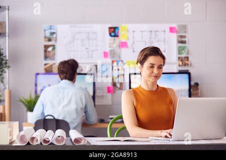 Architetti maschili e femminili in ufficio che lavorano alla scrivania su computer portatili e desktop Foto Stock