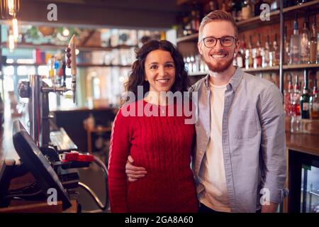 Ritratto di una coppia sorridente che possiede Bar in piedi dietro al bancone Foto Stock
