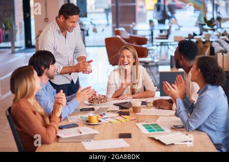 I colleghi celebrano il compleanno di Businesswoman al Meeting Around Table nel moderno ufficio Open Plan Foto Stock