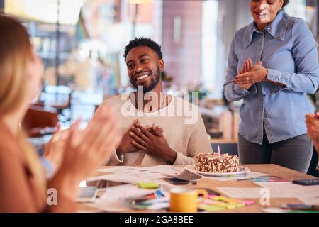 I colleghi celebrano il compleanno di un uomo d'affari al Meeting Around Table nel moderno ufficio a piano aperto Foto Stock