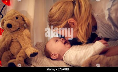 Amorevole Madre coccolante Baby Son sdraiato su coperta in casa accampamento nella camera da letto del bambino a casa Foto Stock