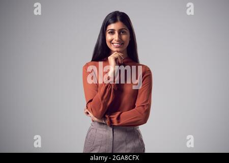 Studio Ritratto di sorridente giovane Businesswoman con Chin appoggiato sulla mano contro sfondo piano Foto Stock