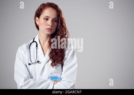 Studio Ritratto di giovane donna stressata Dottore indossando camice bianco contro sfondo normale Foto Stock