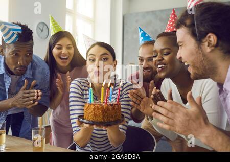 Donna felice che soffia candele sulla torta di festa circondata da amici allegri Foto Stock