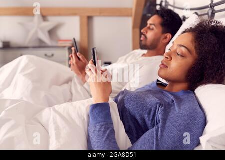 Coppia nel indossare Pajamas addicted ad usare i telefoni cellulari sdraiati nel letto e non comunicare Foto Stock