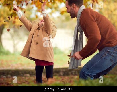 Giovane ragazza che getta l'autunno lascia in aria come ha divertimento giocando in giardino con i genitori Foto Stock