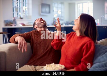 Uomo che cattura popcorn in bocca come Donna lo getta a lui seduto su divano Foto Stock