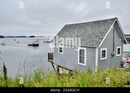 Un cottage grigio sovrasta il porto e si affaccia sulla spazzata di barche di aragosta in una città di pescatori nella costa del Maine. Foto Stock