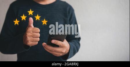 Il cliente tiene in mano lo smartphone e cinque stelle con spazio per la copia. Best Excellent Services Rating for Satisfaction.Customer Experience satisfaction con Foto Stock