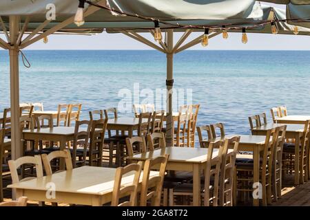 Sedie e tavoli di ristoranti sulla spiaggia pronti per gli ospiti con vista sul mare aperto Foto Stock