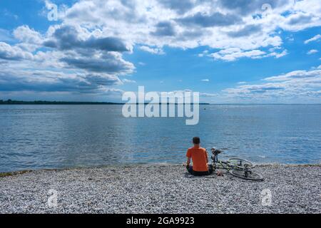 Lachine, CA - 4 luglio 2021: Uomo seduto su ciottoli guardando il lago di Saint Louis Foto Stock