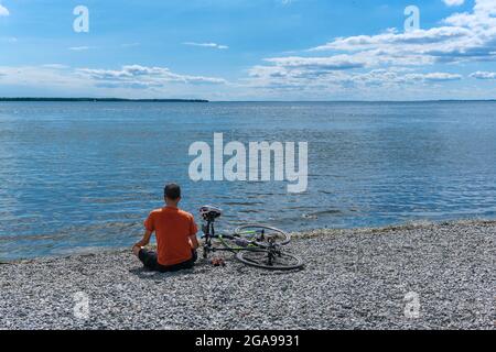 Lachine, CA - 4 luglio 2021: Uomo seduto su ciottoli guardando il lago di Saint Louis Foto Stock