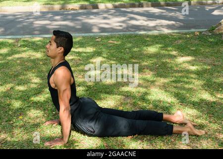 Giovane brasiliano, in posizione di yoga con il cane rivolto verso l'alto, in un parco pubblico in una giornata di sole. Foto Stock