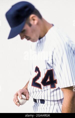 Un giocatore di baseball in uniforme che guarda il baseball in mano. Foto Stock