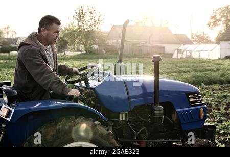 Coltivatore che guida un trattore sul campo. Agroindustria, agroalimentare. Agricoltura, agricoltura. Campagna terreni agricoli. Piccole aziende agricole. Lavorare in agricoltura Foto Stock