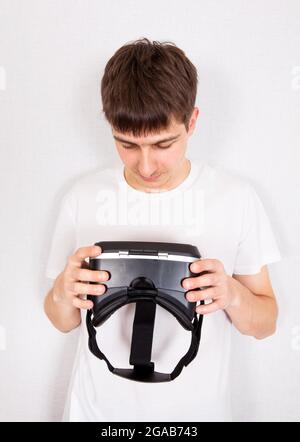 Young Man con Virtual Reality Headset vicino alla parete nella stanza Foto Stock