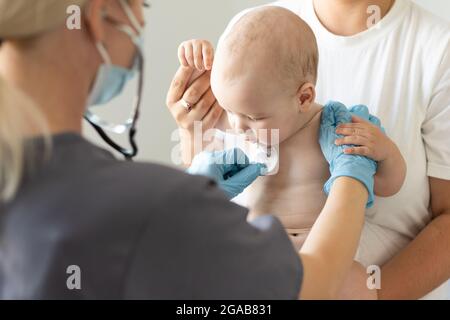 Femmina medico che esamina la bambina piccola sorridente, tenuta dalla madre Foto Stock