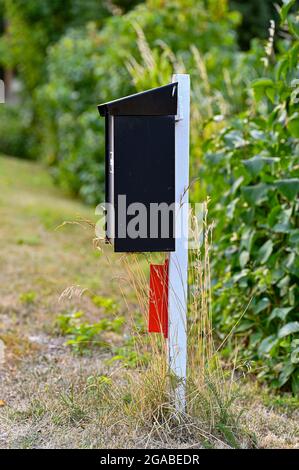 cassetta postale nera su palo di legno bianco vicino alla siepe Foto Stock