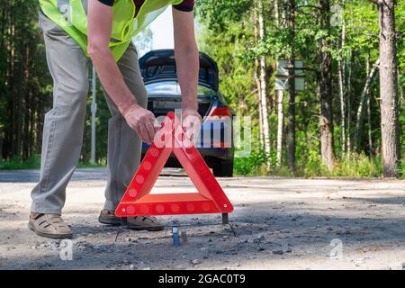 Un uomo adulto mette un triangolo rosso riflettente triangolare di avvertimento Foto Stock