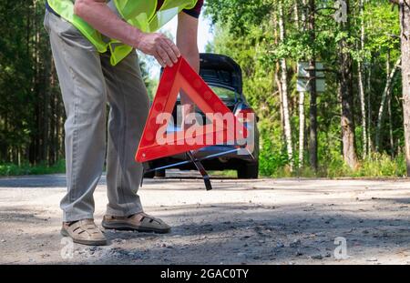 Un uomo adulto mette un triangolo rosso riflettente triangolare di avvertimento Foto Stock