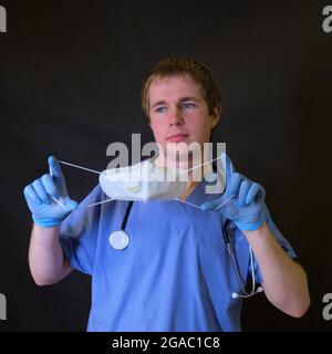 Medico con una cicatrice del respiratore sul viso N95 ffp2 in mano su uno sfondo scuro Foto Stock