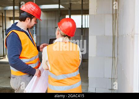 Architetto e artigiano con progetto e computer tablet sul cantiere per la costruzione di una casa Foto Stock