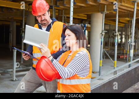 Architetto con computer tablet e operai edili come caposquadra di fronte alla conchiglia sul cantiere Foto Stock