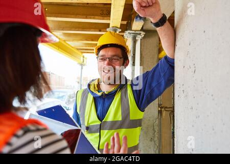 Sorridente artigiano e architetto sul cantiere della casa di costruzione discutere il progetto di costruzione Foto Stock